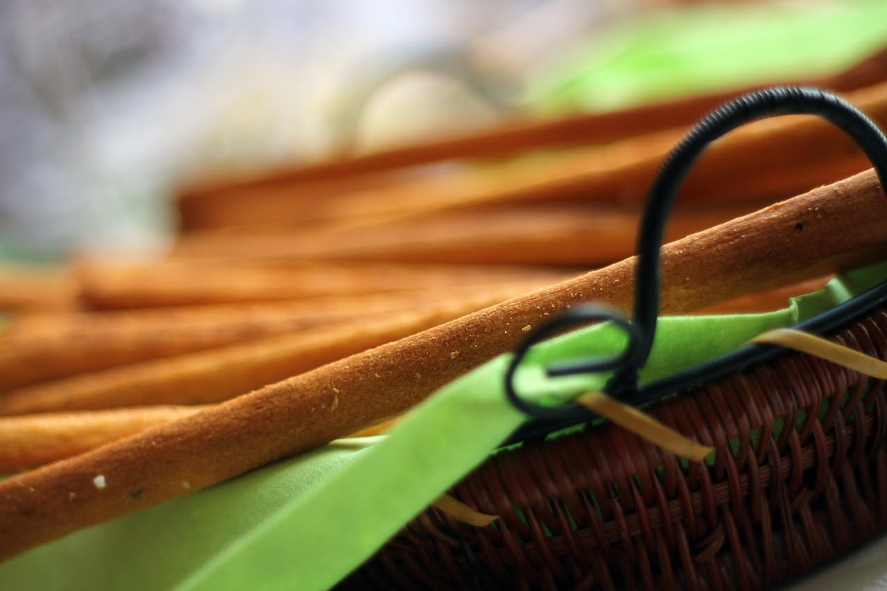 Grissini dorati e croccanti disposti su carta forno accanto a fette di pane raffermo, con una ciotola di olio e rosmarino sullo sfondo