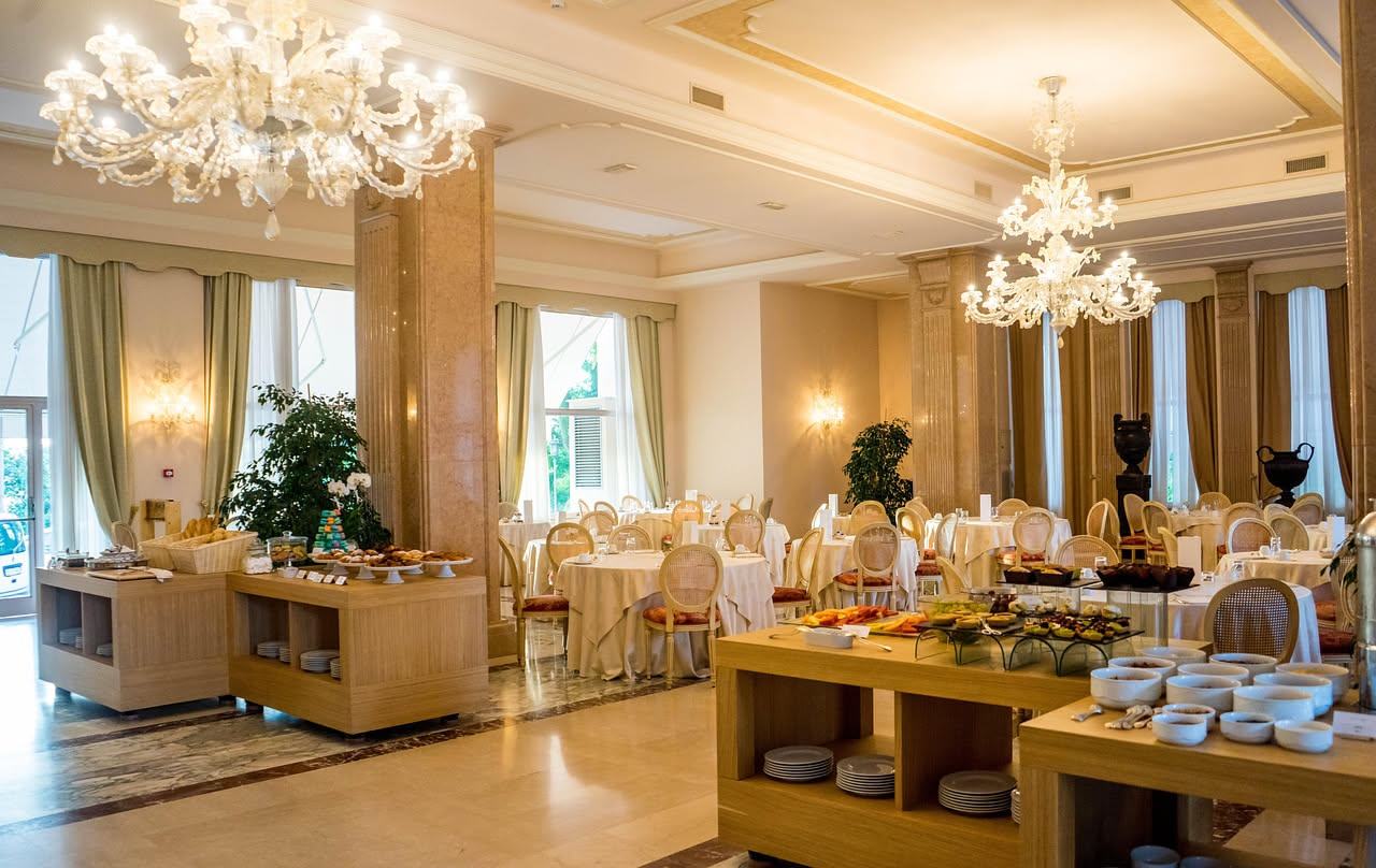 Lampadario in vetro trasparente e cristallo colorato di Murano con pendagli a goccia, sospeso in un salotto con pareti chiare e luce naturale pomeridiana che illumina i cristalli