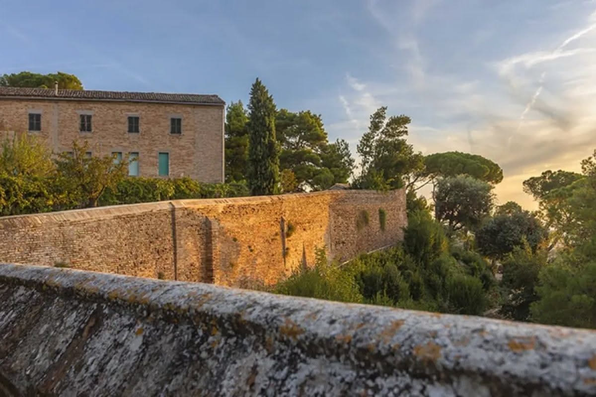 Facciata di villa bianca in marmo bianco statuario con finestre azzurre, vista frontale con giardino mediterraneo, montagne apuane sullo sfondo