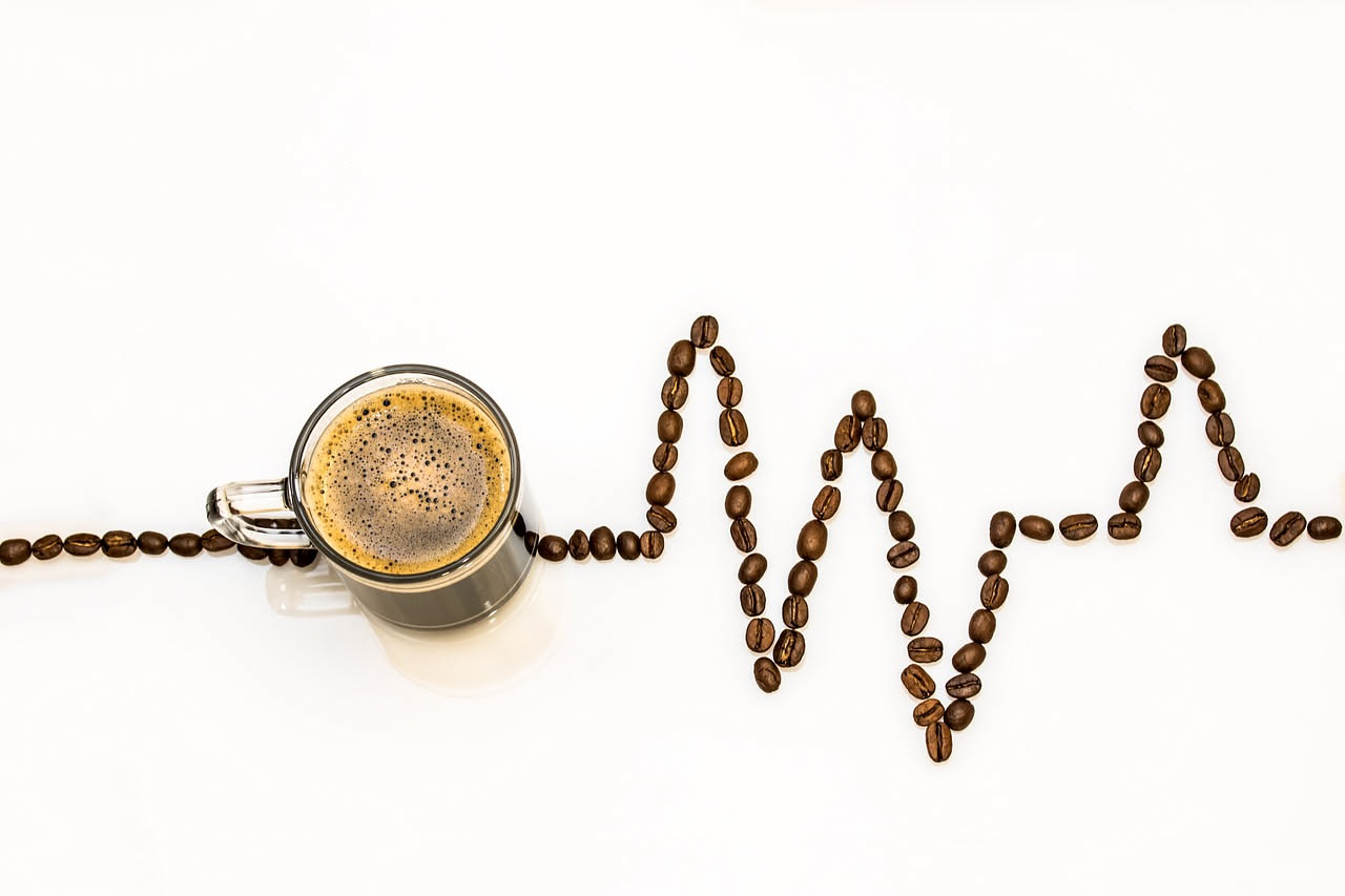 Chicchi di caffè verde in un vassoio accanto a chicchi torrefatti scuri, con sfondo di una torrefazione artigianale illuminata da luce naturale