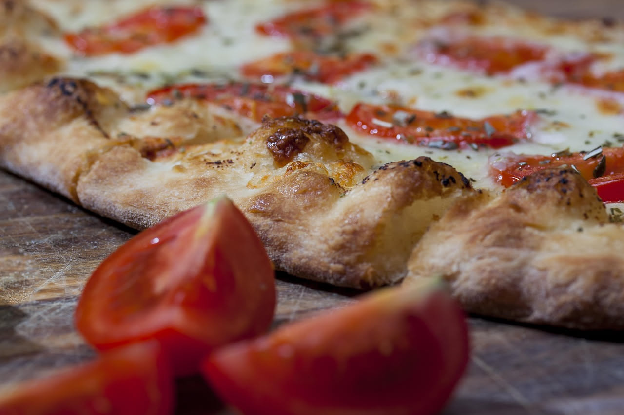 Focaccia dorata e croccante cosparsa di sale grosso e rosmarino fresco su una teglia di carta forno, con una trama uniformemente soffice e bordi croccanti