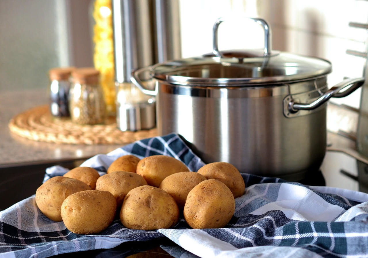 Pentola con acqua torbida lattiginosa ancora calda, patate dorate a lato, in cucina con piante verdi sullo sfondo