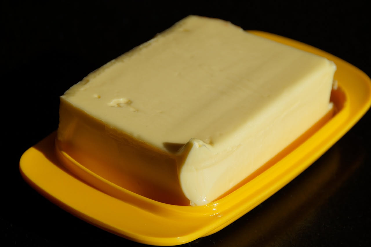 Burro di cocco bianco in ciotola di ceramica accanto a panetto di burro animale giallo pallido su piano di marmo bianco con sfondo neutro