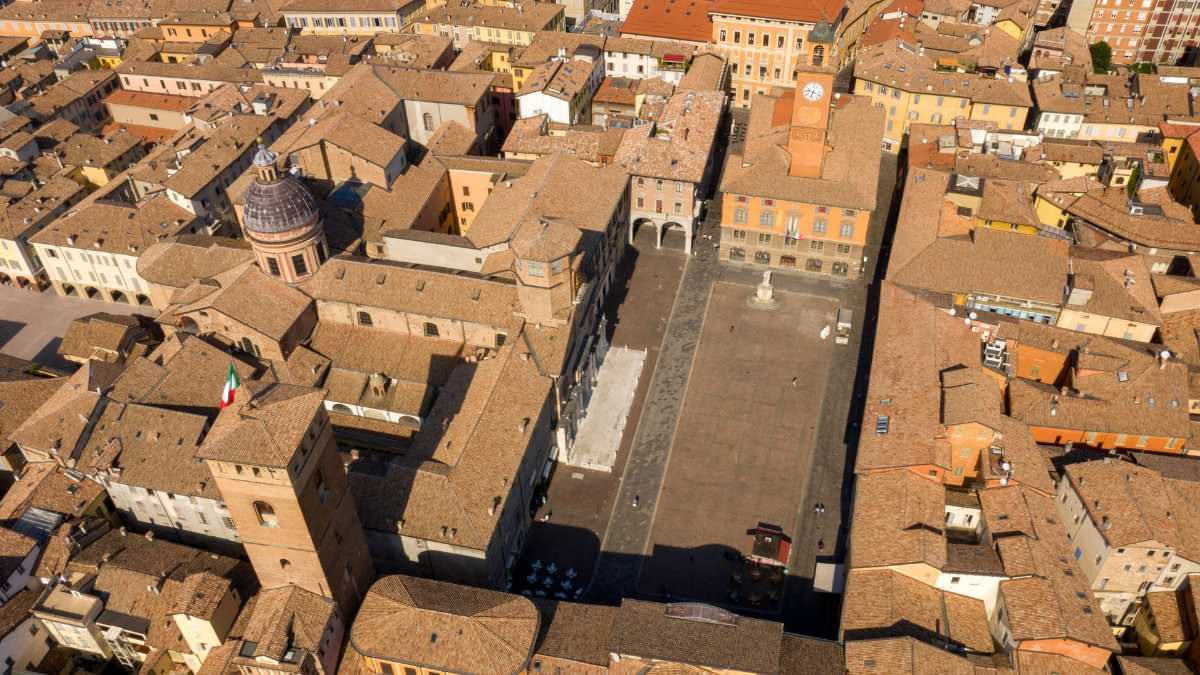Cascina rurale in cotto rosso con tetto di coppi, circondata da campi di pianura in Emilia-Romagna, muri spessi e finestre piccole tipiche del periodo rurale