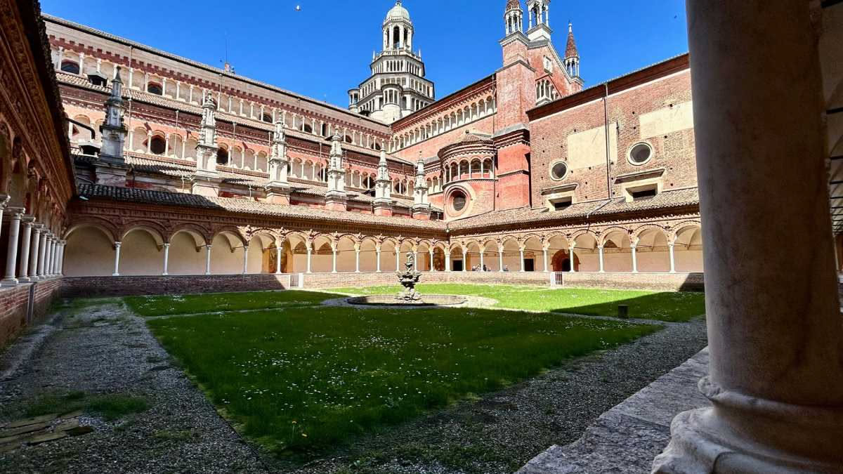 Cortile interno genovese con fontana in pietra chiara, muri di mattone rosso consumato dal tempo, vegetazione rampicante negli angoli, luce diffusa dal cielo ristretto in alto