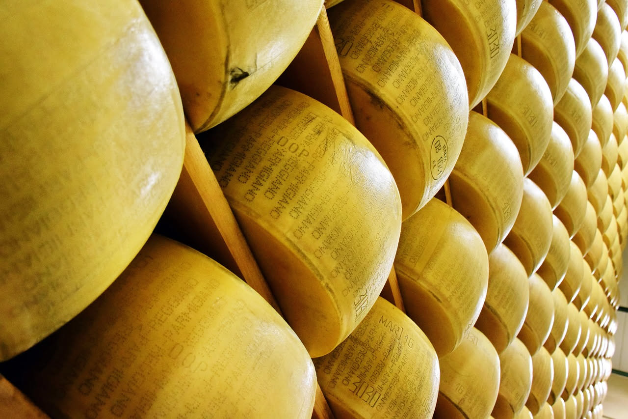 Una forma di Parmigiano Reggiano invecchiato con incisioni laterali nella cantina di stagionatura, sullo sfondo altre forme in file ordinate su scaffali di legno