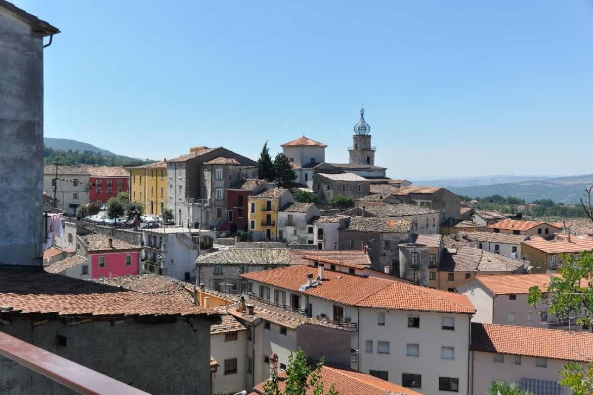 Tetto in laterizio rosso di una casa storica in borgo toscano con coppi tradizionali, tegole curve e piccole riparazioni visibili, montagne sullo sfondo, luce pomeridiana