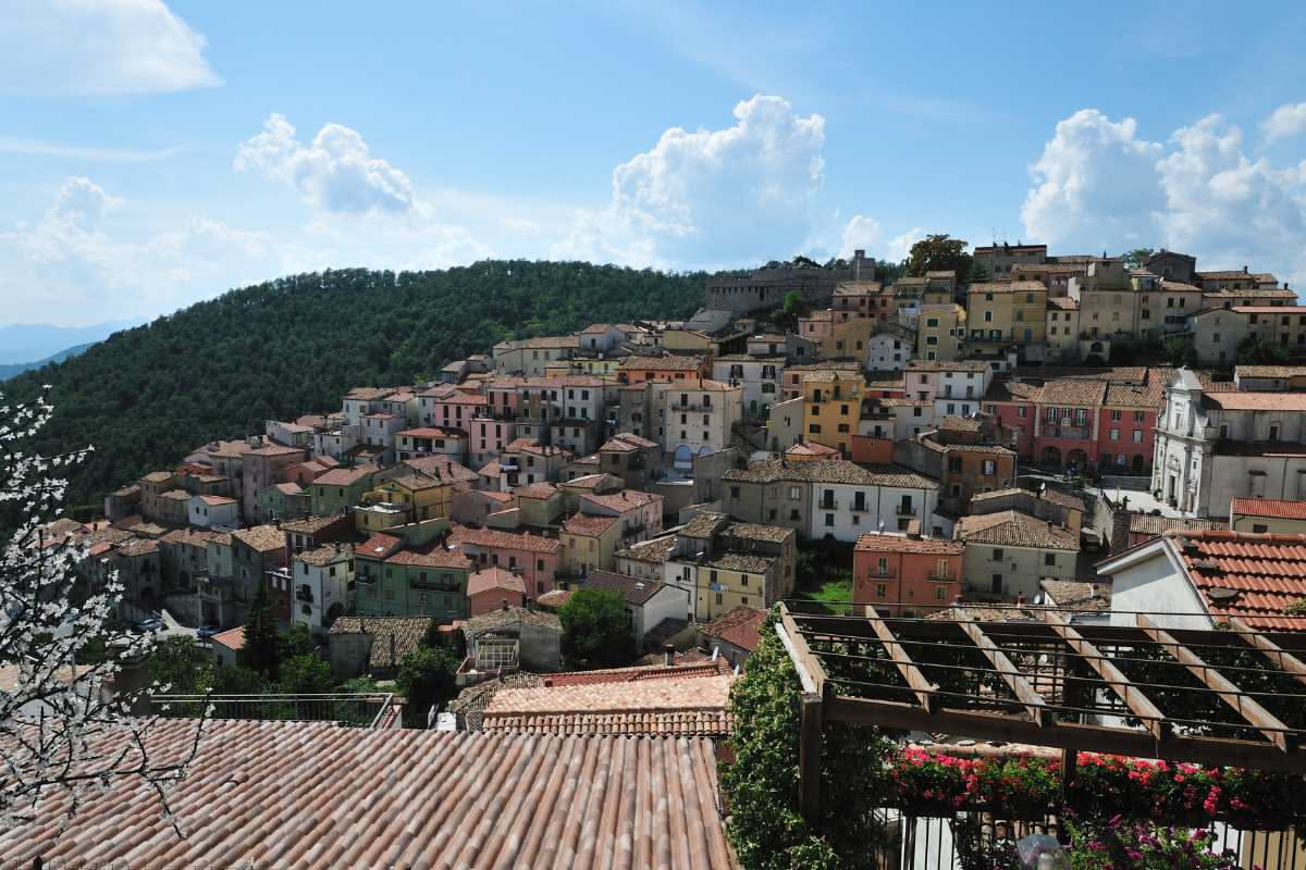 Tetti di coppi rossi su casette di pietra in un borgo toscano, con tegole curve che si sovrappongono sotto la luce del tramonto, sullo sfondo colline verdi ondulate