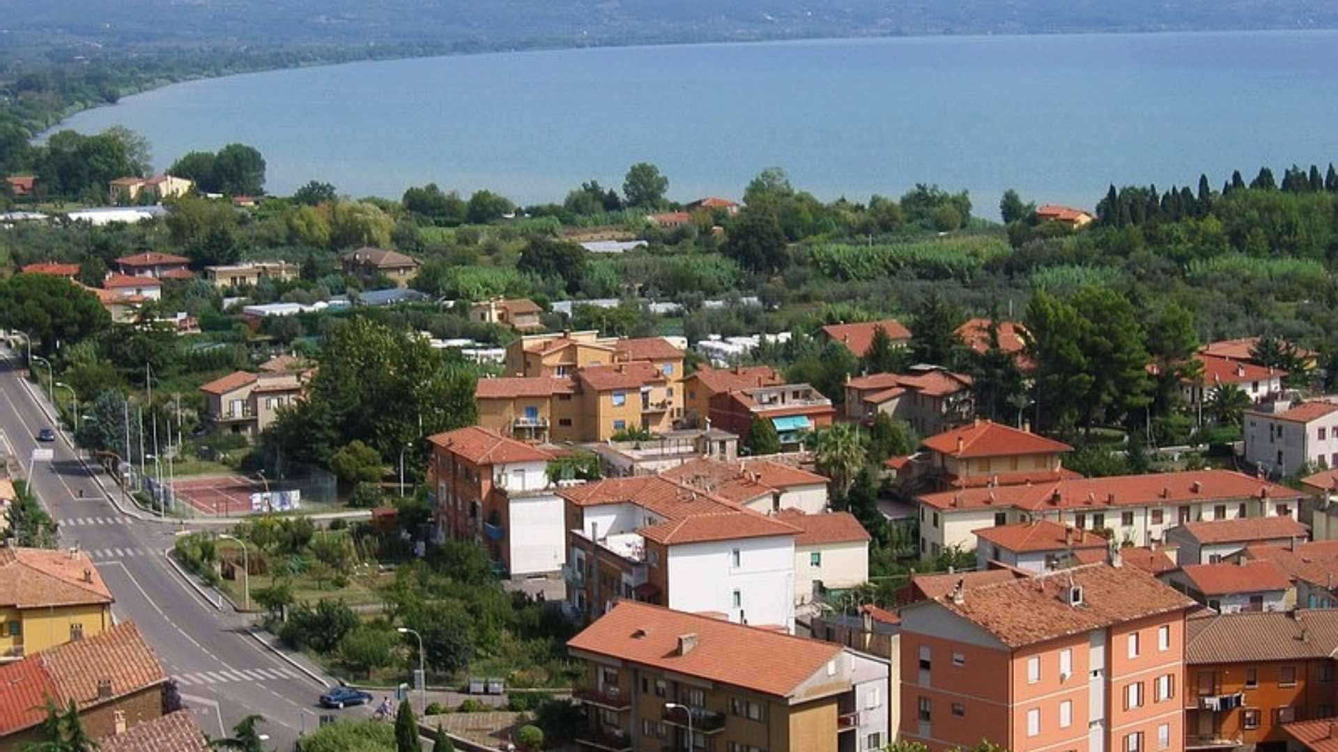 Tetto di casa rurale in laterizio con grondaie in rame, cisterna in muratura sotterrata visibile in primo piano, terreno di campagna intorno, cielo nuvoloso