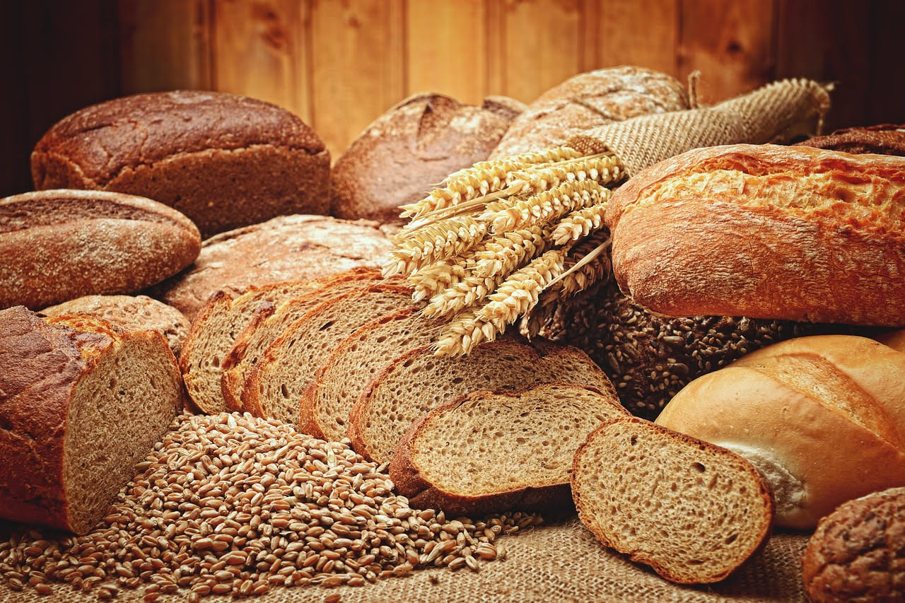 Spighe di grano dorato in un campo italiano, con un mulino in pietra sullo sfondo e una bottiglia di acqua di sorgente accanto a una pagnotta di pane toscano