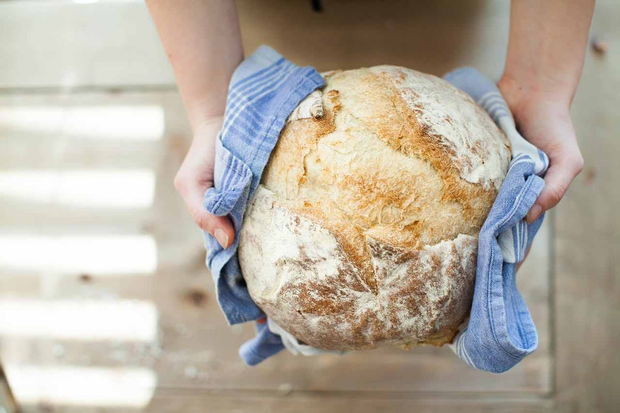 Pane toscano appena sfornato, crosta dorata e croccante, tagliato a fette su una tavola di legno con chicchi di grano e farina bianca accanto