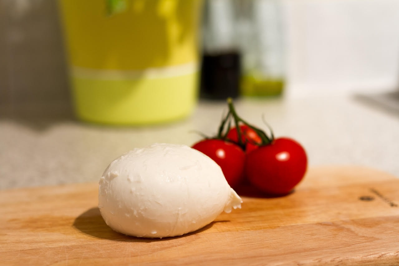 Mozzarella fresca bianca in ciotola di ceramica con siero di latte, lato una bottiglia di latte intero locale e sfondo di campagna della Piana di Sele con mucche al pascolo