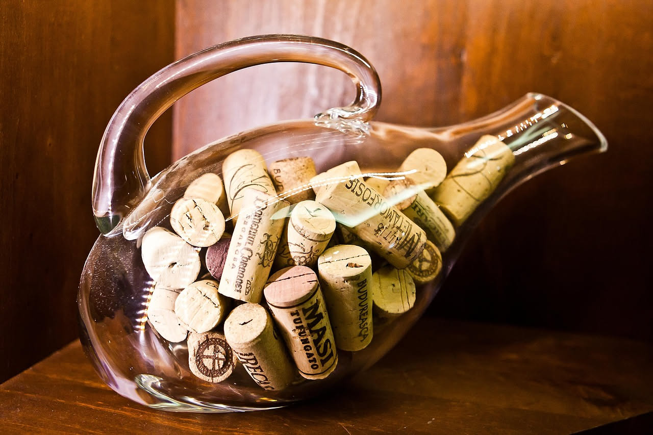 Bottiglie di vino vuote di colore verde e marrone trasformate in vasi per piante, lanterne decorative e dispenser per liquidi su una superficie di legno naturale