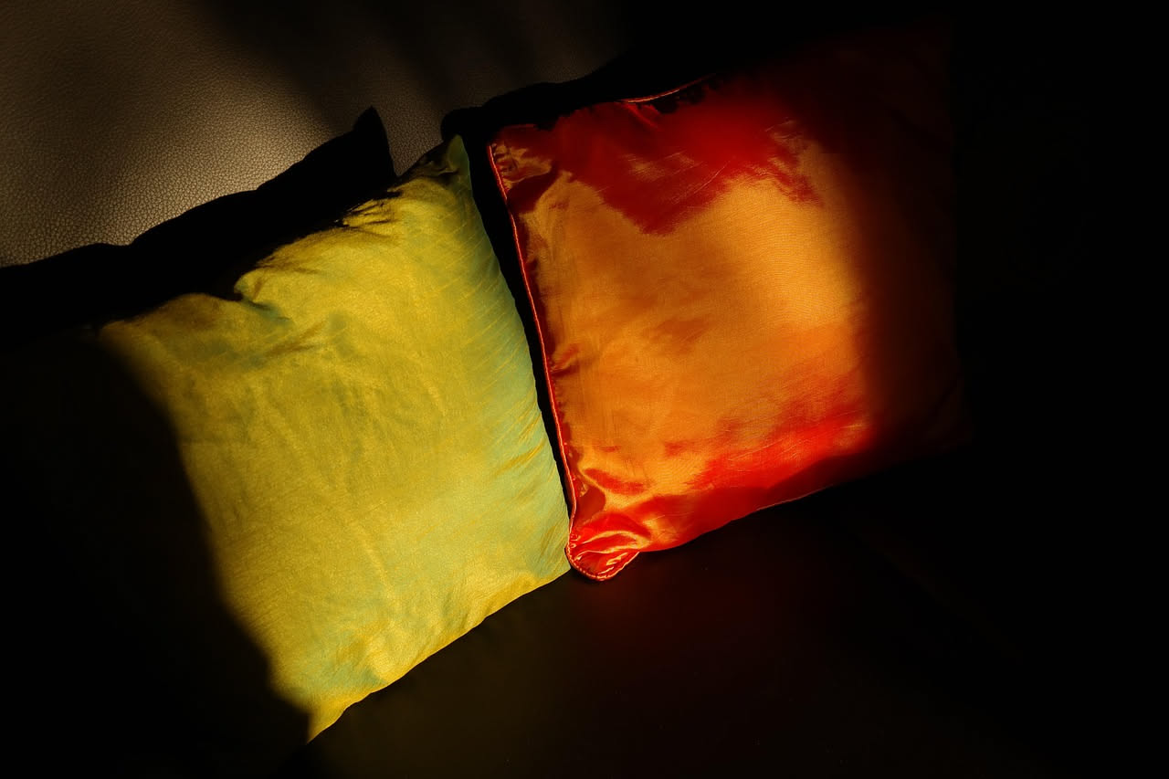 Cuscini colorati e deformati accatastati su un tavolo, con ago e filo, forbici e rotoli di stoffa per il riuso creativo