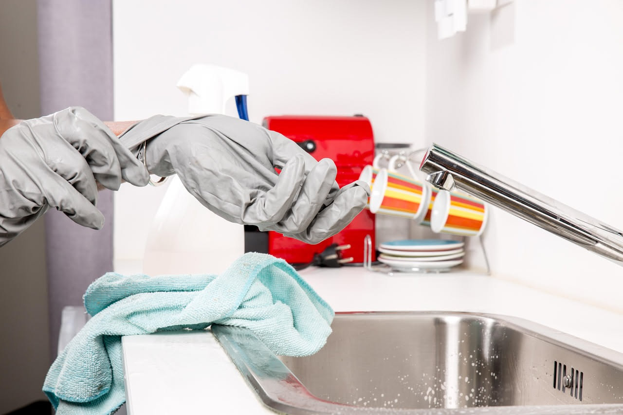 Mobili da cucina in legno chiaro con grasso accumulato, accanto a una spugna, bottiglie di aceto bianco e bicarbonato di sodio per la pulizia naturale