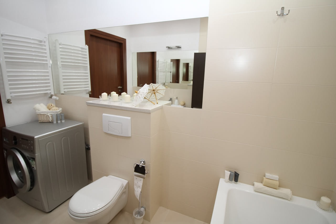 Bagno moderno con lavabo bianco, wc e bidet, con bottiglia di aceto trasparente posizionata su un ripiano in marmo, accanto a uno strofinaccio di cotone naturale