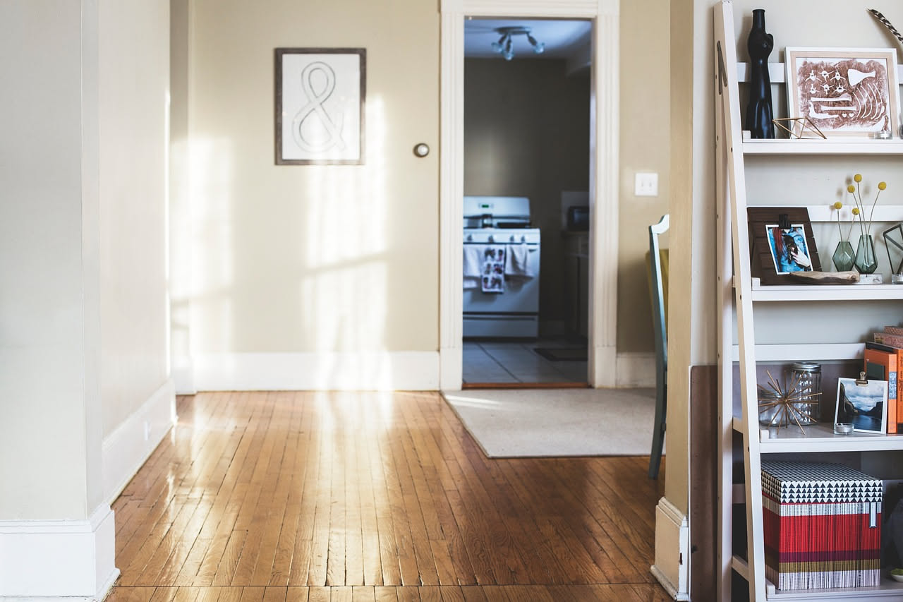 Pavimento in parquet di legno chiaro con riflessi luminosi, un panno in cotone bianco e una ciotola di legno contenente una miscela di pulizia naturale accanto a una spazzola morbida.