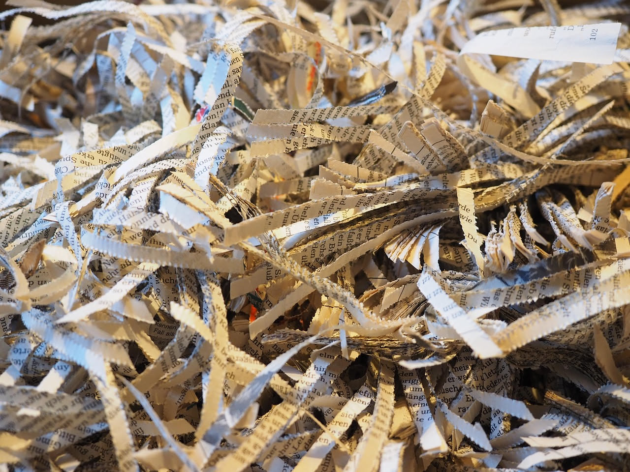 Stack ordinato di giornali piegati in bianco e nero con titoli leggibili, accanto a forbici, colla e fogli di carta colorata per progetti di riciclo