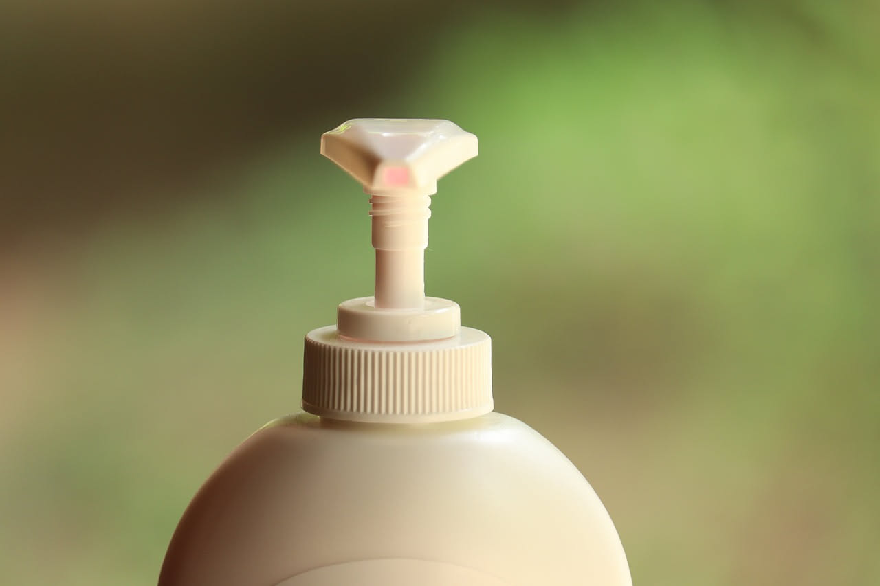 Contenitori di detersivi vuoti in plastica trasparente e opaca disposti in fila, accanto a forbici, pennarelli e materiali per il riutilizzo creativo