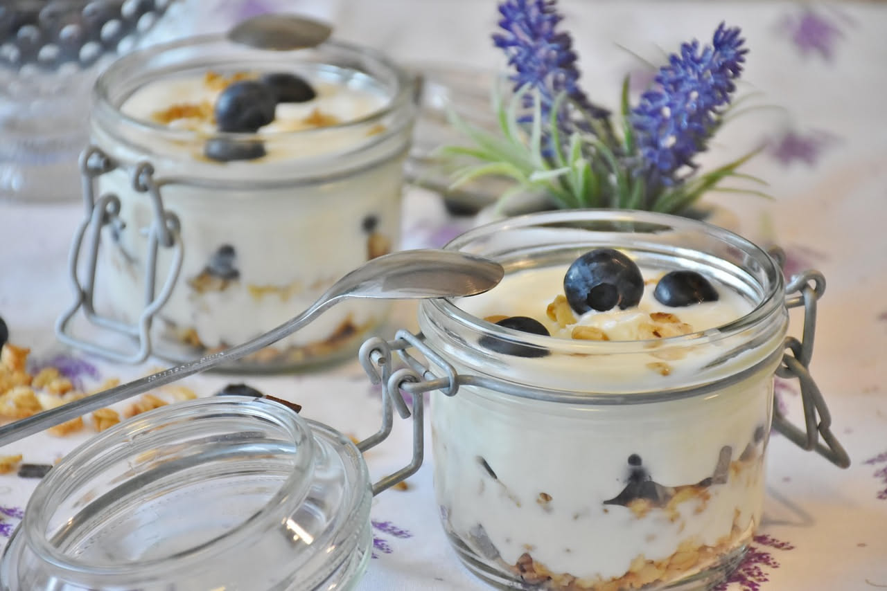 Vasetti di yogurt trasparenti di diverse dimensioni, alcuni ripieni di semi, terriccio e piantine verdi, altri utilizzati come organizzatori da cucina con pasta e riso