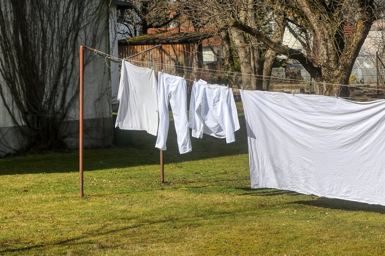 Mucchio di vecchi lenzuoli in cotone bianco e colorato piegati su un tavolo di legno con forbici e ago accanto