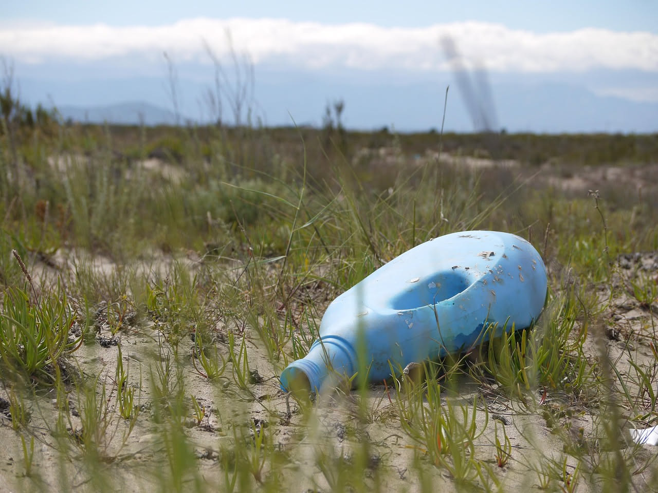 Tre bottiglie di plastica colorate vuote di detersivo poste su un tavolo di legno con accanto spugne, panno di cotone e spray pulito