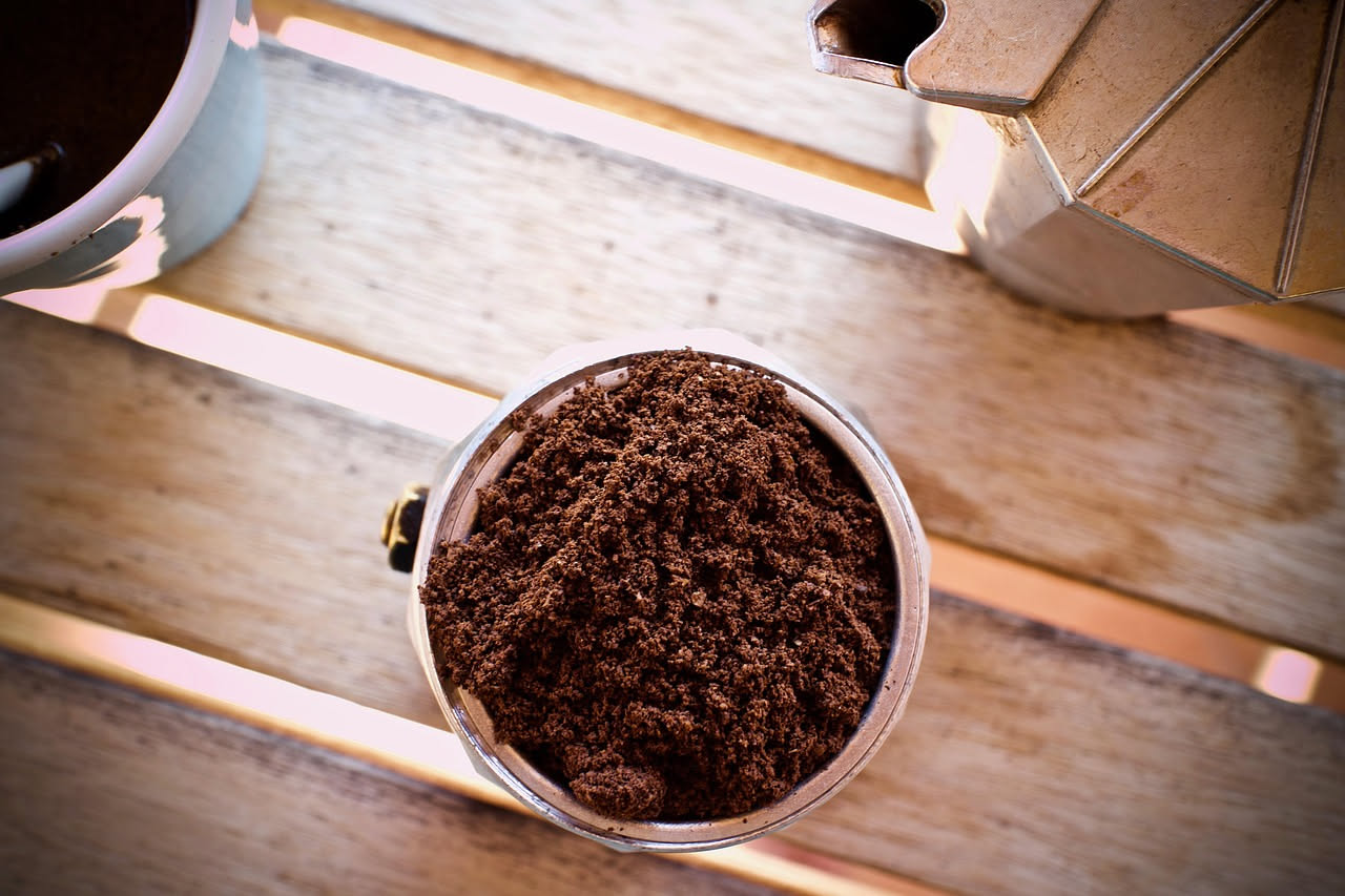 Caffettiera moka spaccata in due parti con depositi calcarei biancastri visibili all'interno, accanto a una tazza di caffè, aceto bianco, limone e bicarbonato