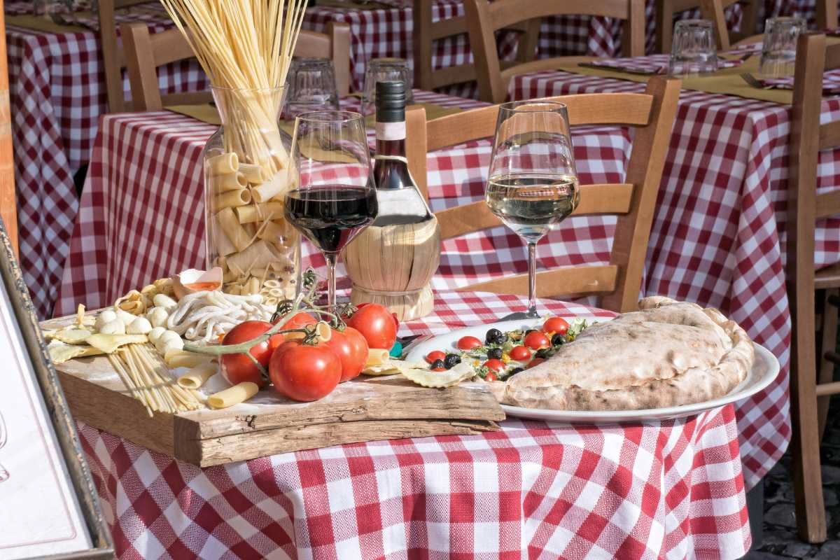 Tovaglia bianca con macchia di vino rosso, accanto bicarbonato in ciotola bianca, limone tagliato a metà e bottiglietta di aceto bianco su tavolo di legno