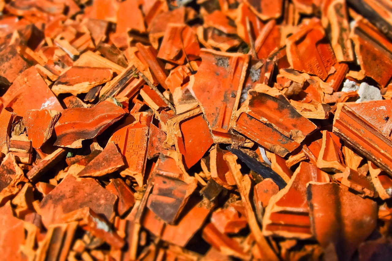 Vaso di terracotta rotto in frammenti su una superficie di legno, accanto a una pianta verde e attrezzi da giardinaggio