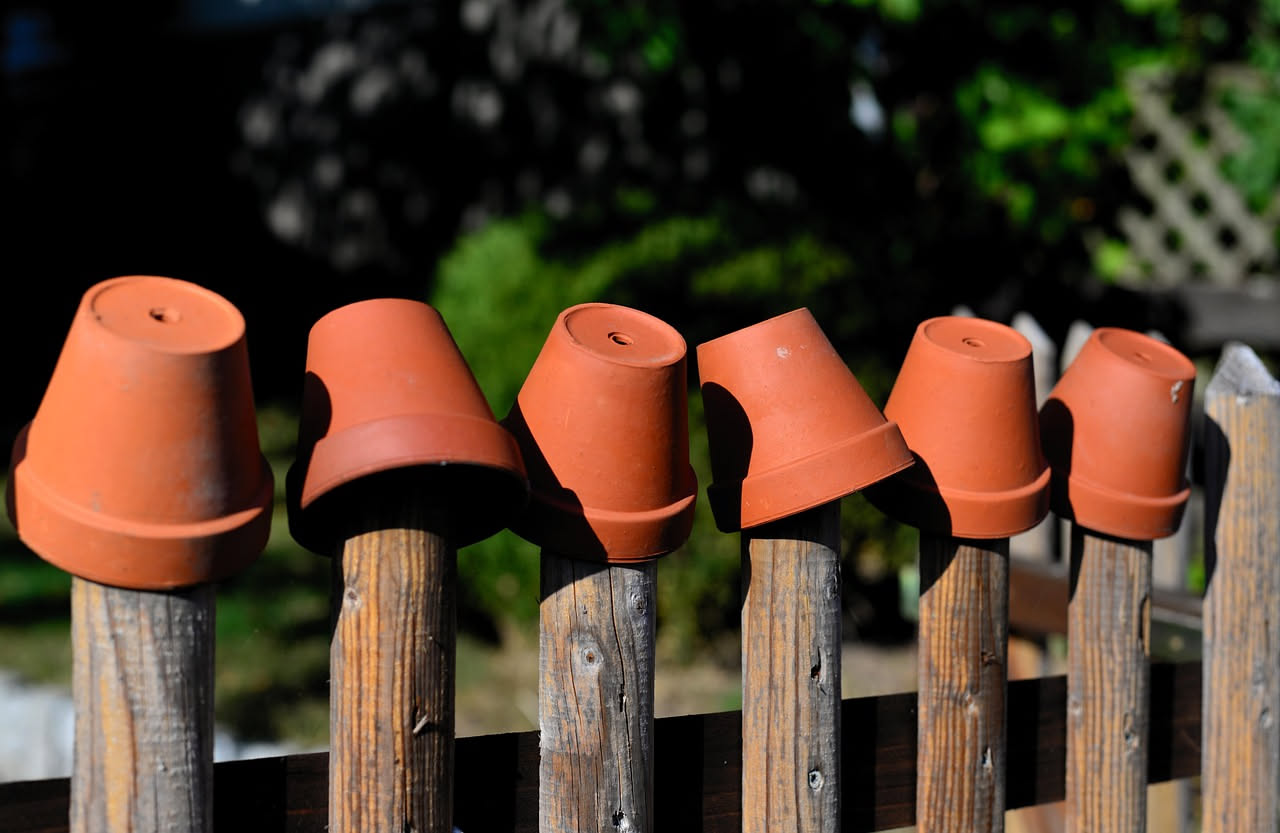 Vasi di terracotta puliti e luminosi su un balcone con gerani rossi e tracce d'acqua che asciugano al sole