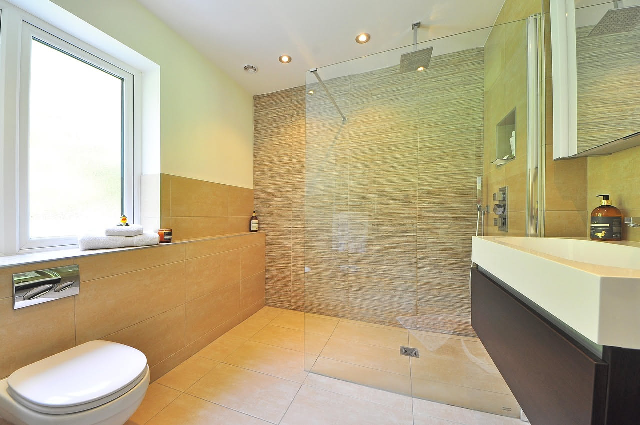 Bagno moderno con specchio appannato, piastrelle umide e finestra chiusa; raggi di sole estivo entrano dalla finestra