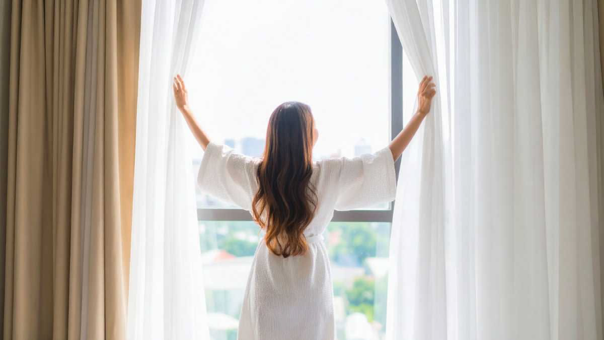 Tende bianche e leggere appese a una finestra luminosa con raggi di sole che le attraversano, con una ciotola di bicarbonato e limone sul davanzale