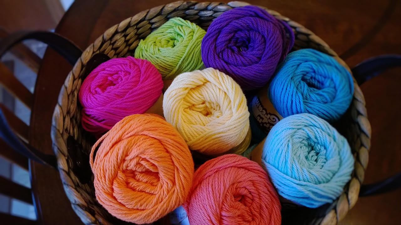 Primo piano di un'etichetta bianca su un gomitolo di filato grigio, con testi e simboli di lavaggio ben visibili, sfondo sfocato di altri gomitoli colorati