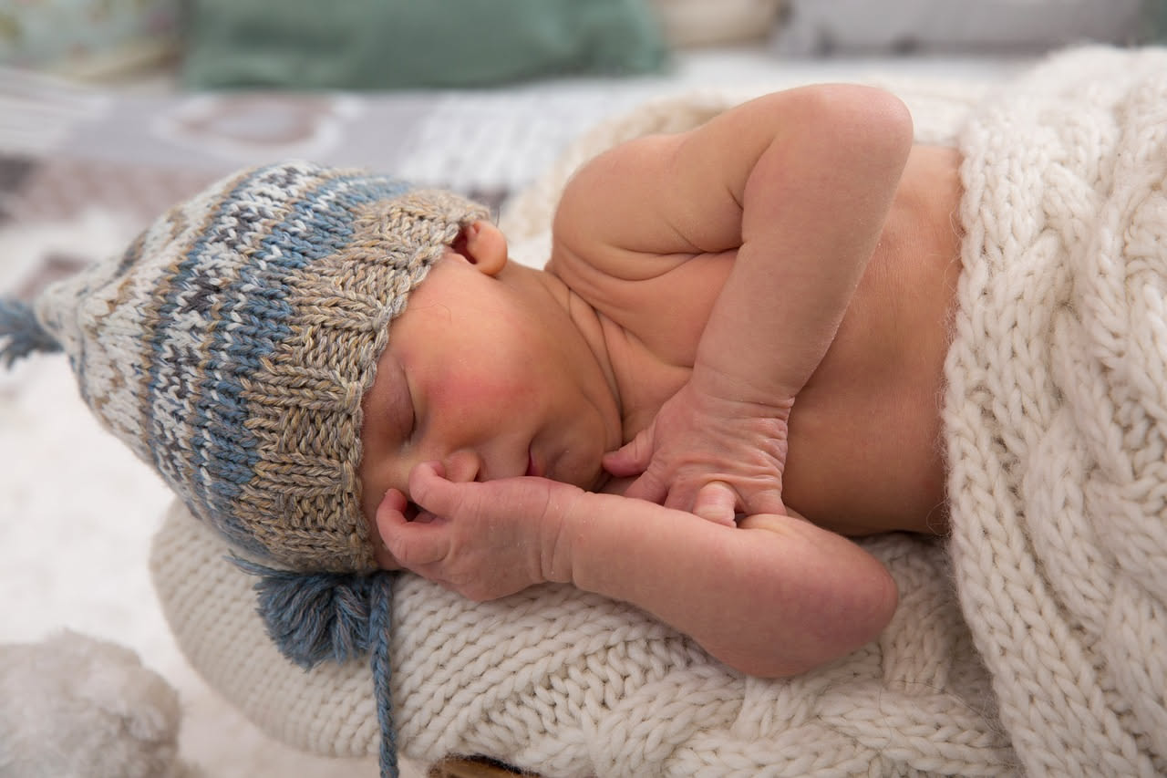 Bambina che si gratta il braccio, indossa un maglione di lana color crema; accanto alcuni gomitoli di filati morbidi disposti su una superficie di legno naturale