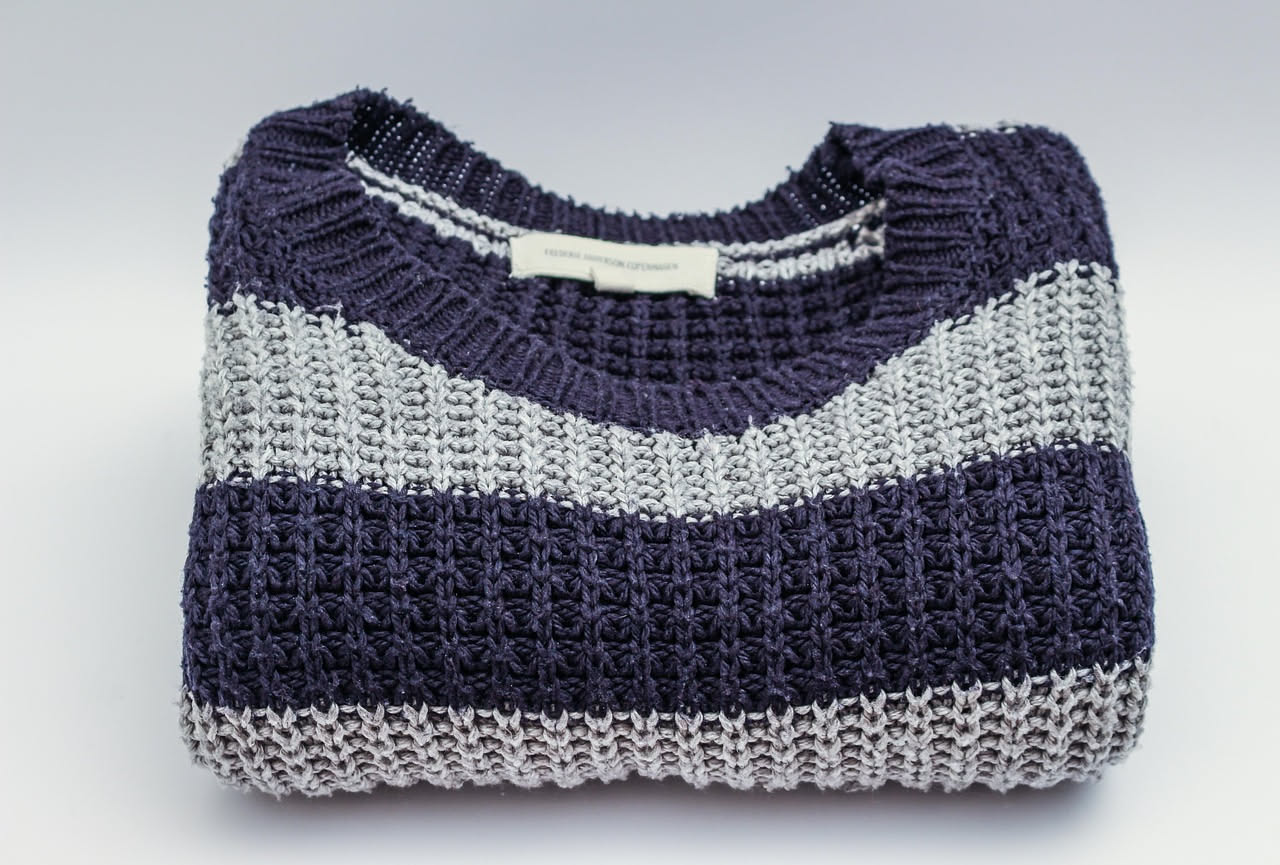 Maglione di lana merino beige ripiegato in un armadio di legno con palline di naftalina poste accanto, accanto un campione di tessuto di lana intatto