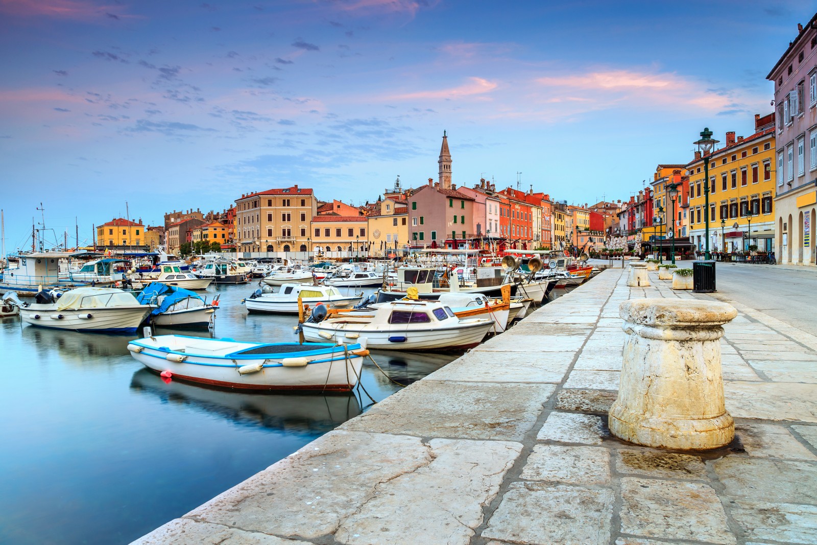 Veduta del centro storico di Rovigno con la chiesa di Sant'Eufemia che domina il promontorio, le case colorate affacciate sul mare e le batane ormeggiate nel porto.